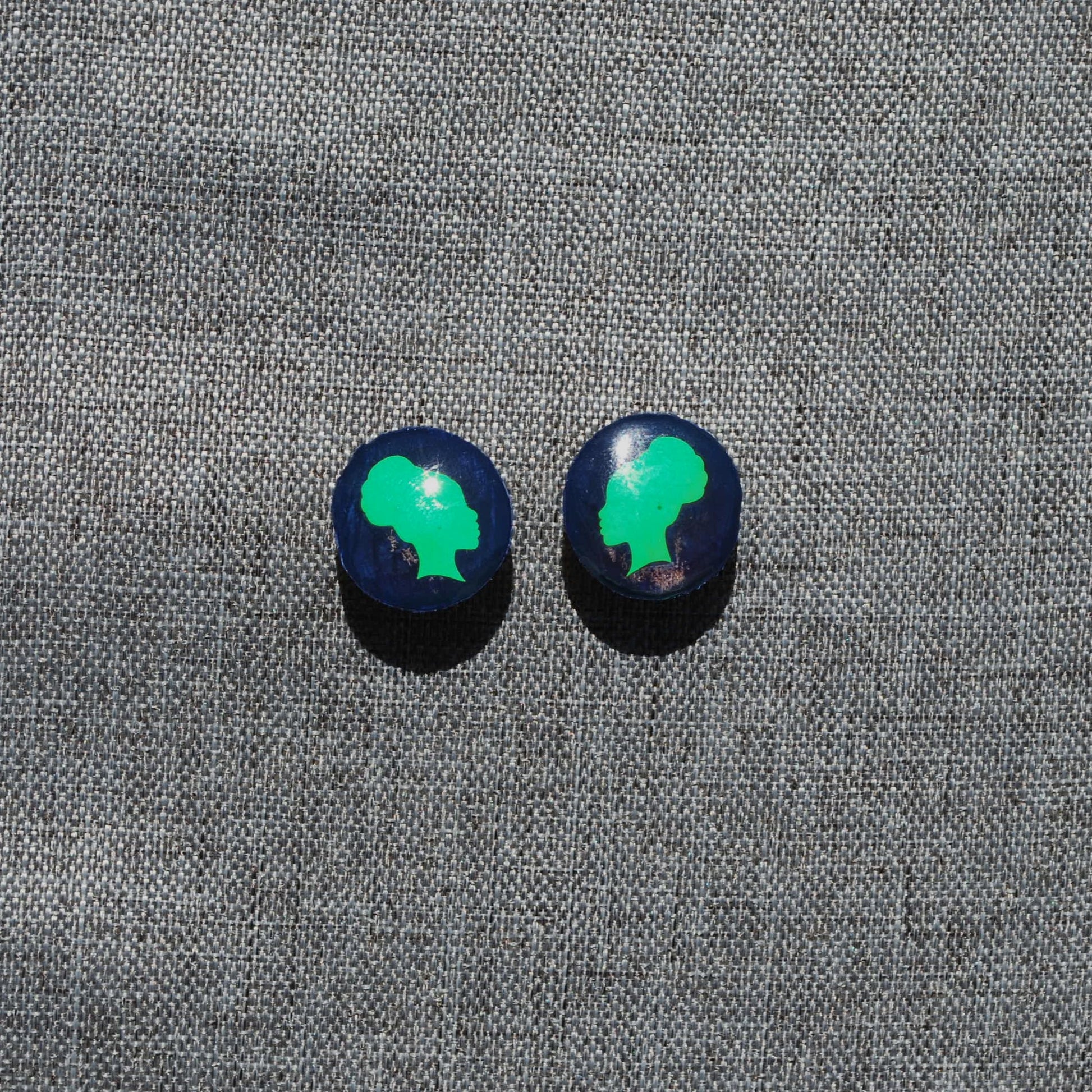 Blue and green 1" diameter round earrings. Blue background with side facing woman with puff ponytail green applique. 