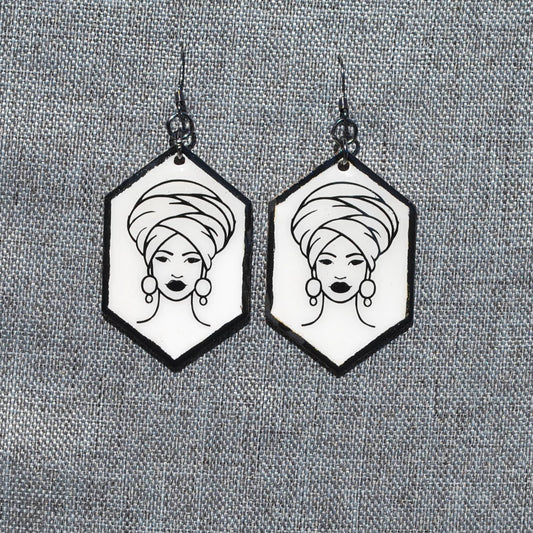 Black and white hexagon earring. White background with black trim. Black outlined woman with head wrap applique.